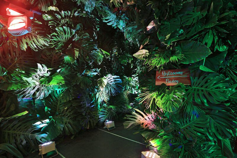 Rotulo de baños sobre pared decorada de hojas tropicales